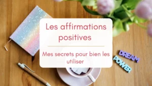 Sur une table en bois, sont posés un vase avec des tulipes roses, une tasse remplie de petits mots, des magnets "dream et power" et un carnet pailleté couleur arc-en-ciel. Image pour illuster les pensées positives.